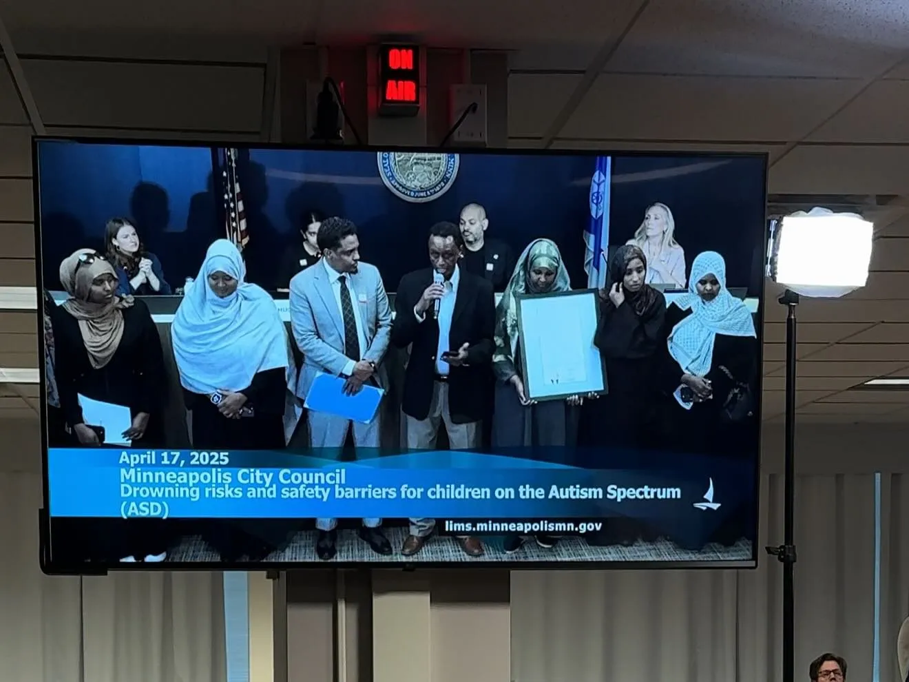 A screen in the Minneapolis City Council chambers shows “April 17, 2025, Drowning risks and safety barriers for children on the Autism Spectrum (ASD).”
