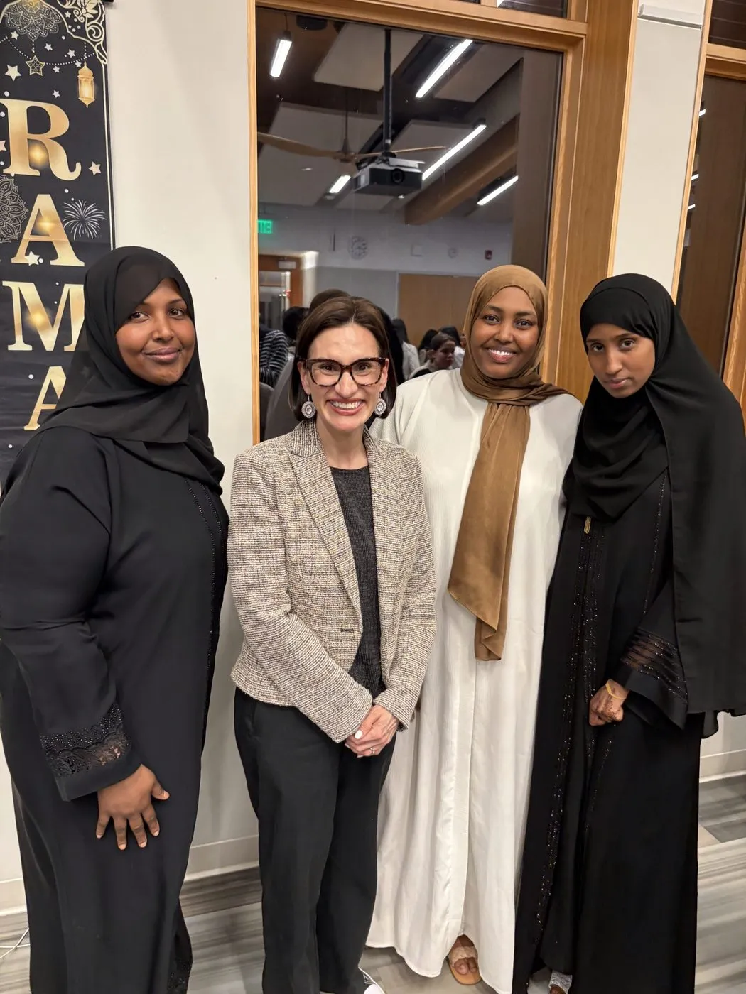 Four women, including a guest in a light blazer, stand together at an event.