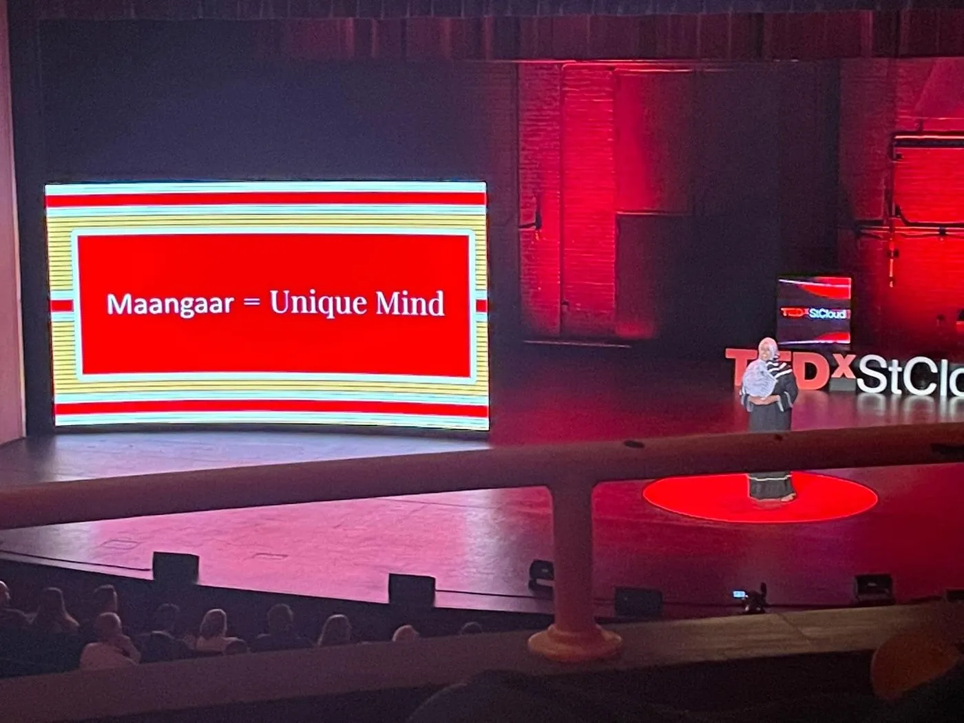 A TEDx stage with a large screen reading “Maangaar = Unique Mind.”