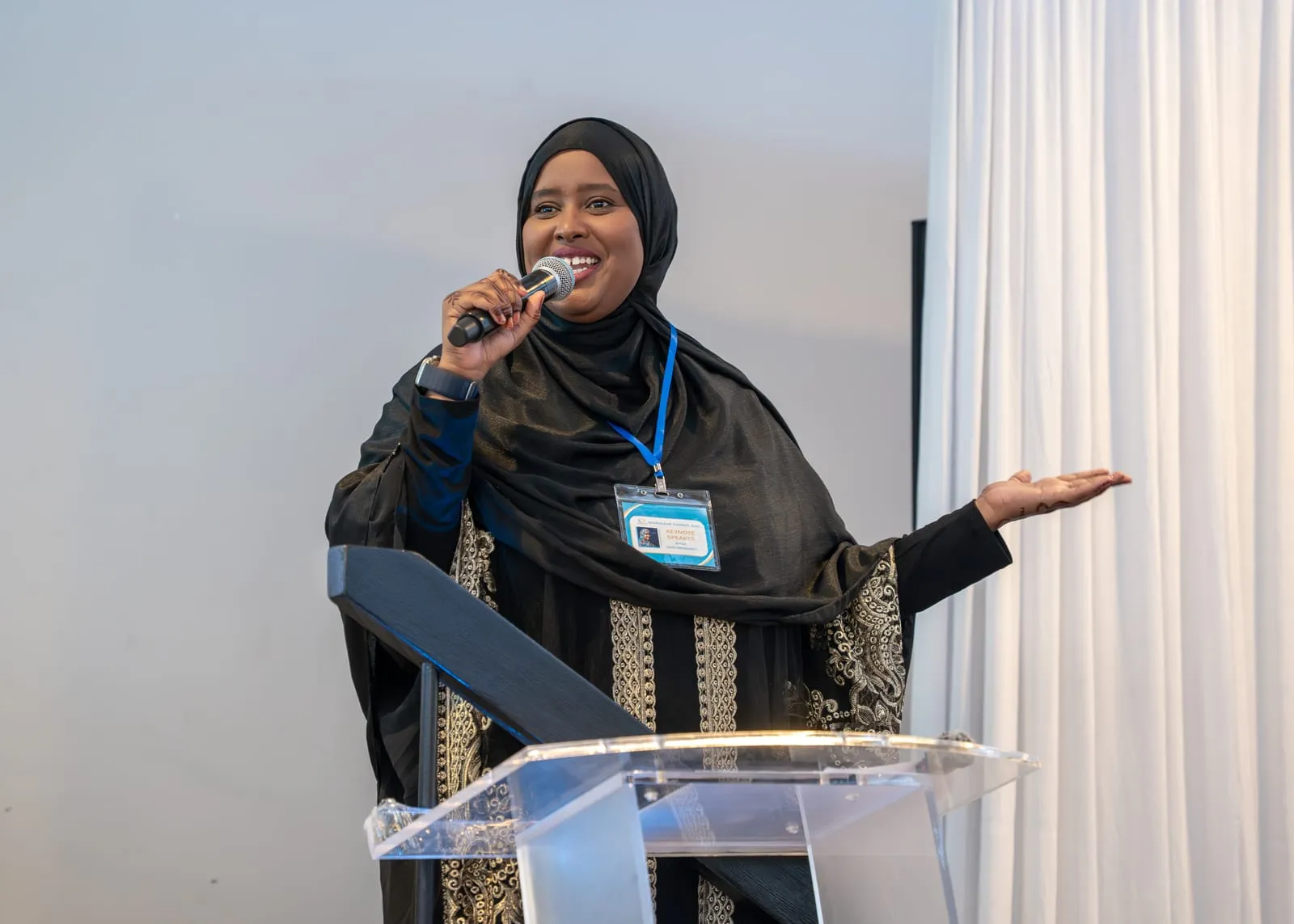 A speaker in a black hijab and embroidered abaya addresses the room from the podium at Maangaar Summit 2025.