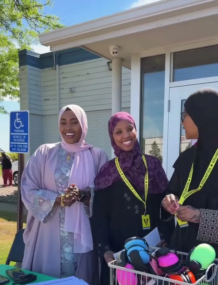 Volunteers in lanyards greet families at the sensory table outside the masjid, with a basket of headphones ready.