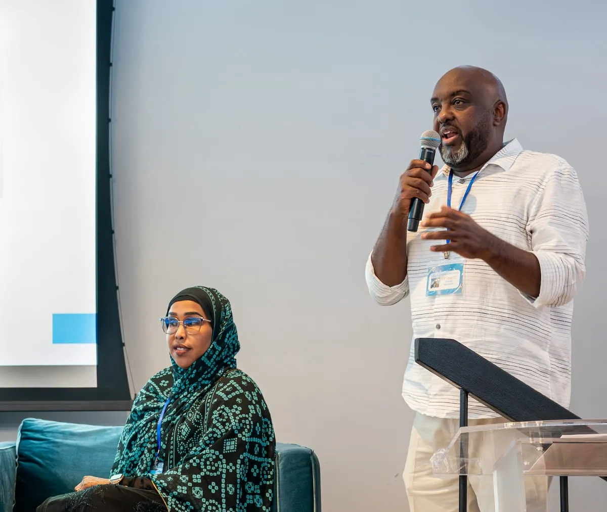 A speaker addresses the room with a microphone while a panelist listens.