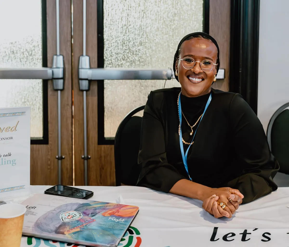 A smiling exhibitor seated at a resource table.