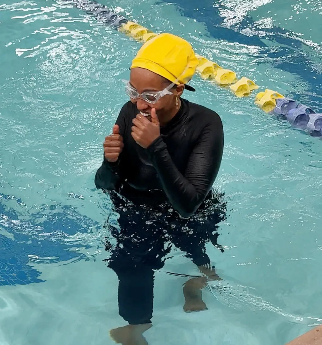 A swim participant in a yellow cap and goggles standing in the pool.